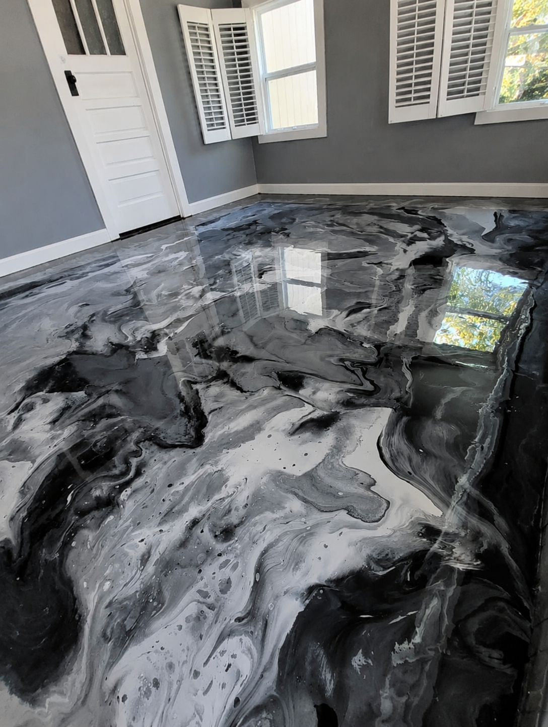 The same sunroom finished with a glossy black, white and silver metallic marble epoxy floor reflecting the windows
