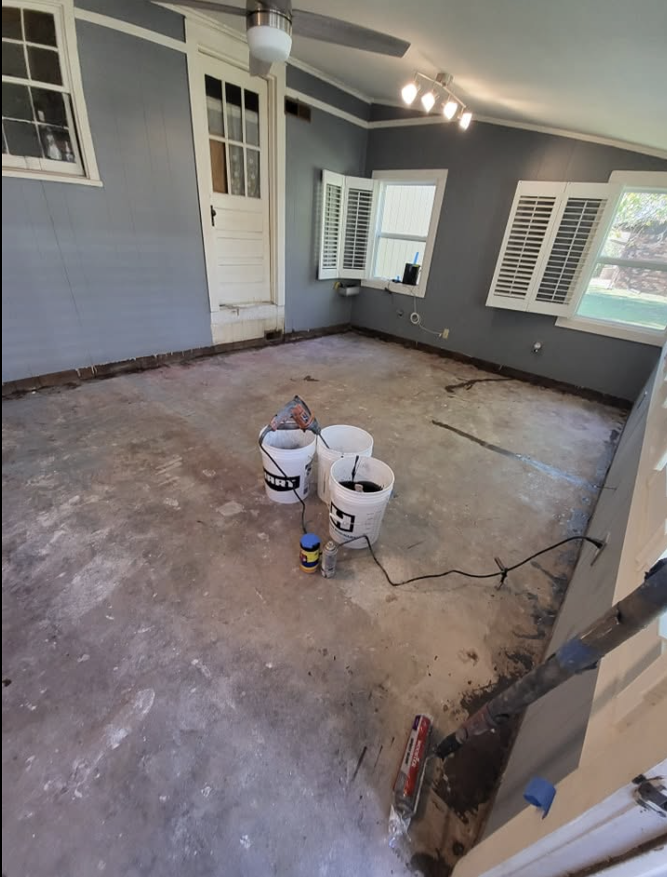 Stripped sunroom with bare, patched concrete subfloor and mixing buckets before the epoxy pour